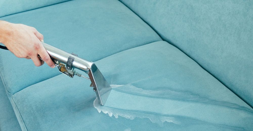 Person Cleaning a Teal Couch with A Cleaning Tool — Totally Green Cleaning Solutions in Belconnen, ACT