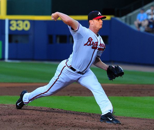 Baseball pitcher in Braves uniform throwing a pitch on the mound, in a stadium.