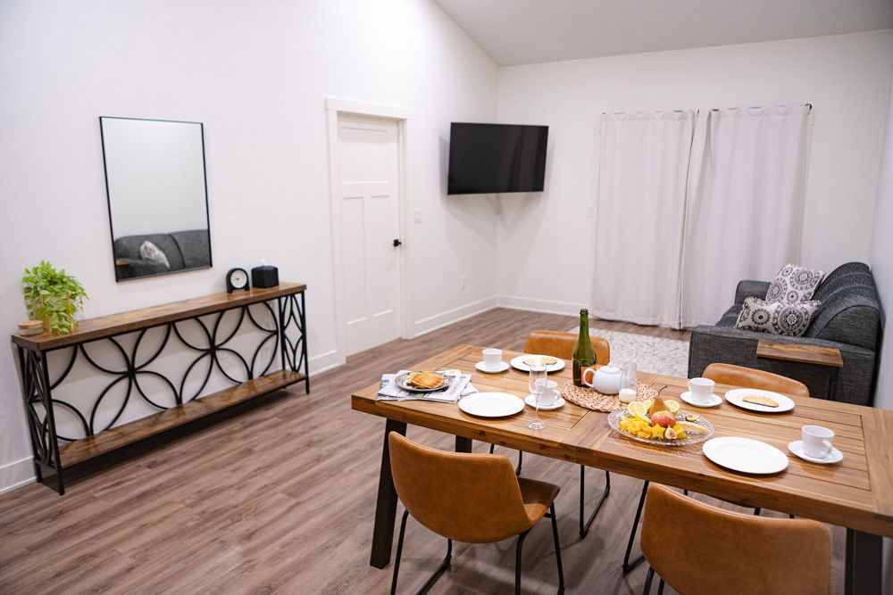 Dining room with set table, wall TV, gray sofa, and decorative console against white walls.