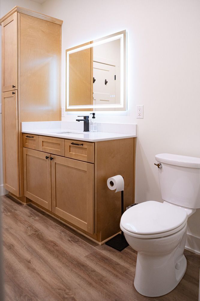 Modern bathroom with wood vanity, mirror, sink, and white toilet on wood-look flooring