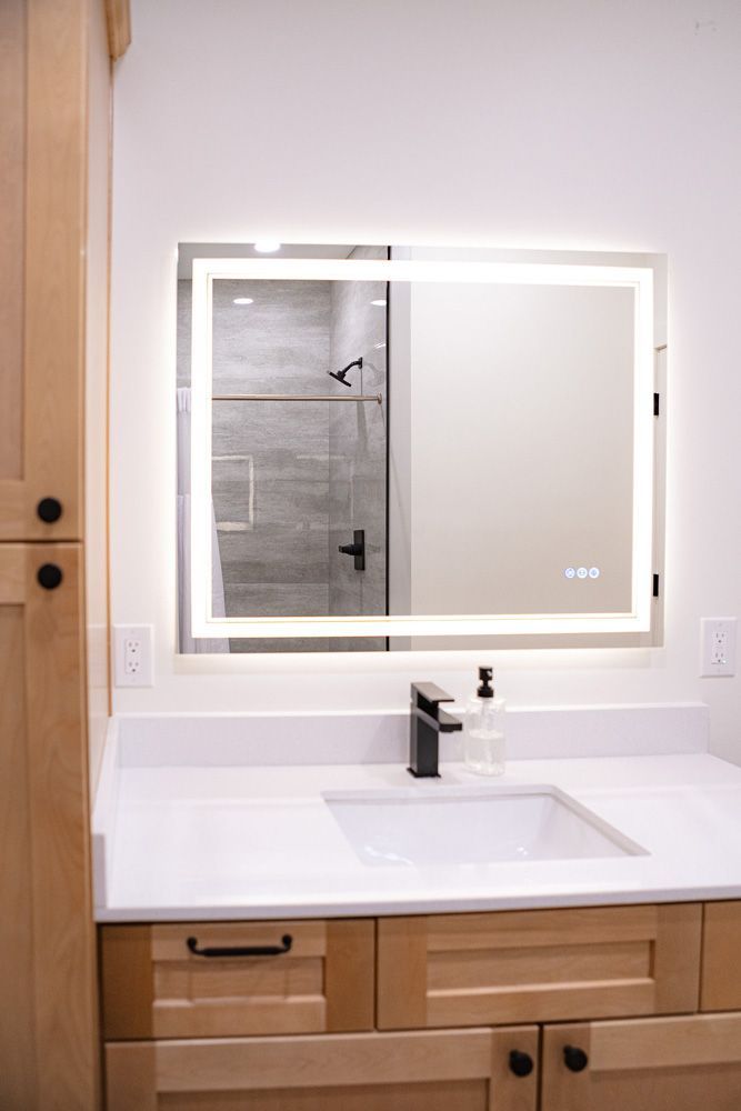 Bathroom vanity with lit mirror, white countertop, and wood drawers under a wall-mounted sink.