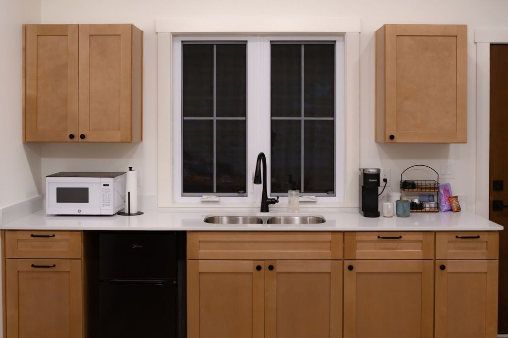 Wooden kitchen cabinets and countertop with sink under a window, microwave on the left, and small appliances on the right