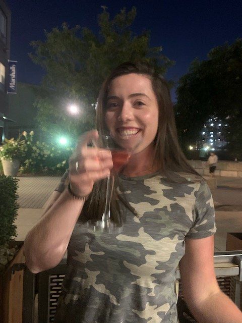 A woman in a camo shirt is holding a glass of wine