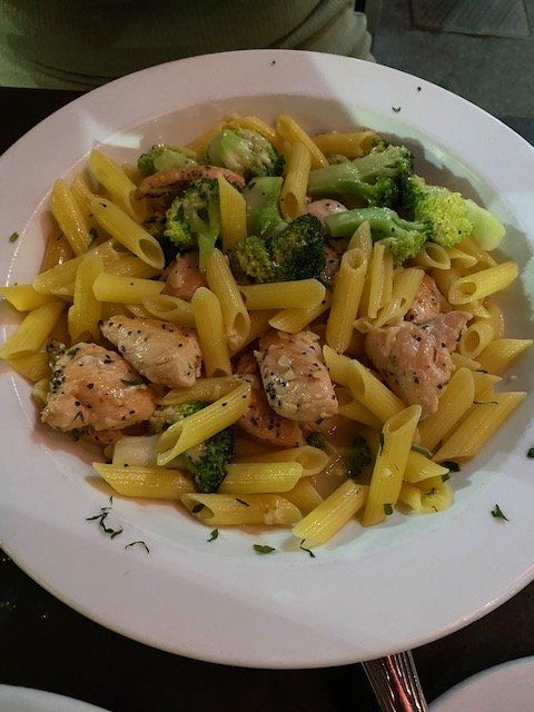 A plate of pasta with broccoli and chicken on a table