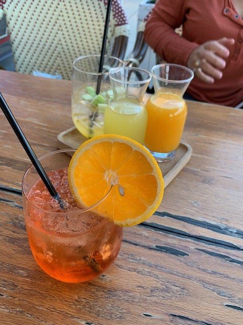 Three drinks are on a wooden table with straws and a slice of orange.