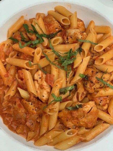 A plate of pasta with chicken and tomato sauce on a table.