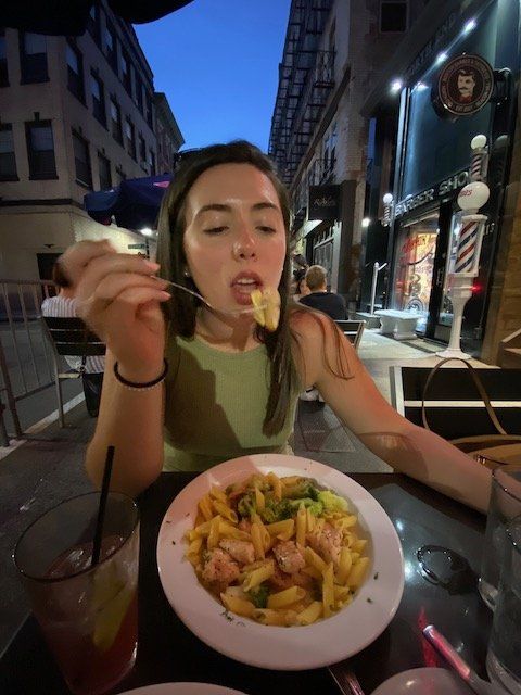 A woman is sitting at a table eating a bowl of pasta