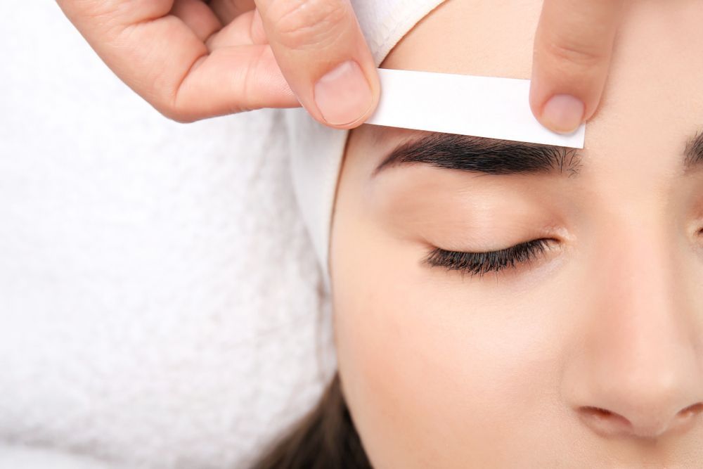 Hands Shaping an Eyebrow With a White Brow Template Over a Closed Eye — Fraser Shores Hair Design in Fraser Coast, QLD