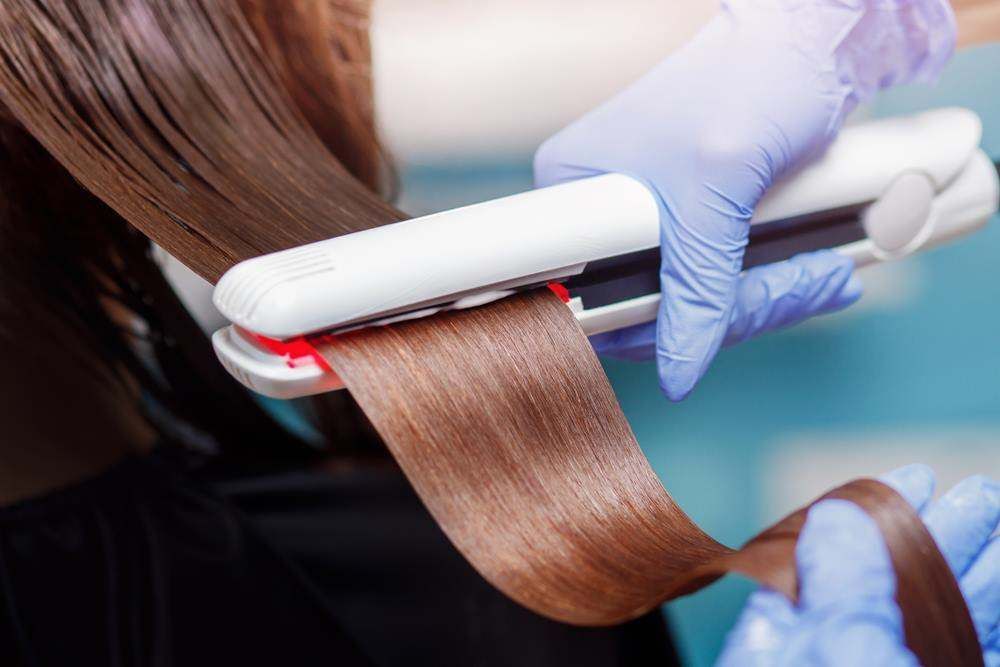 Hair Being Straightened with A White Flat Iron by Gloved Hands, Close-Up View — Fraser Shores Hair Design In Urraween, QLD