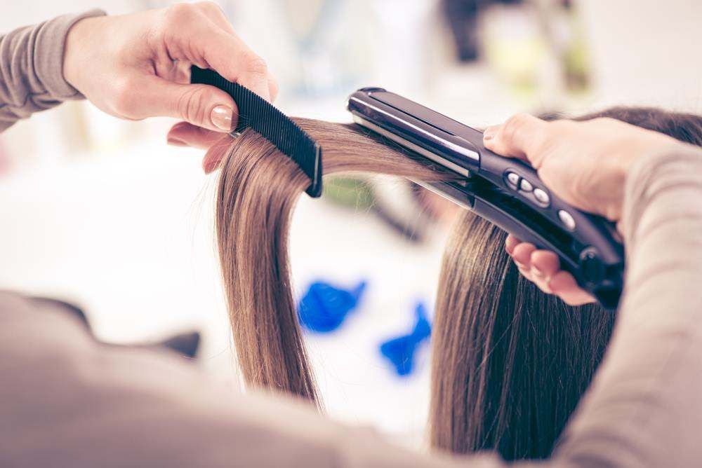 Hairdresser Straightening a Brown Hair Extension with A Flat Iron in A Salon — Fraser Shores Hair Design In Urraween, QLD