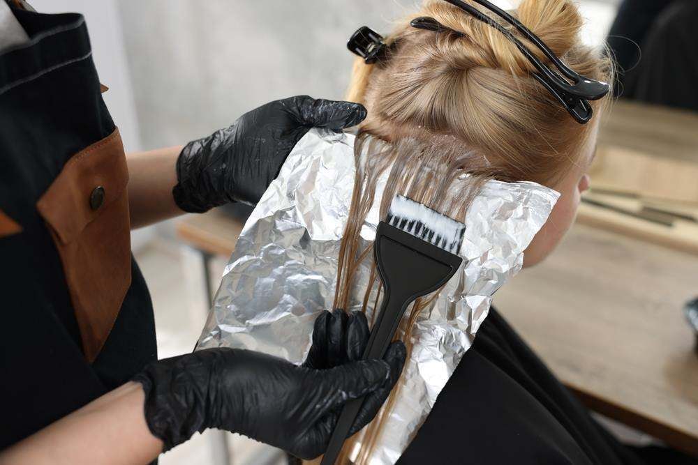 Gloved Hands Applying Hair Dye with A Brush to Foil-Wrapped Blonde Hair — Fraser Shores Hair Design In Urraween, QLD