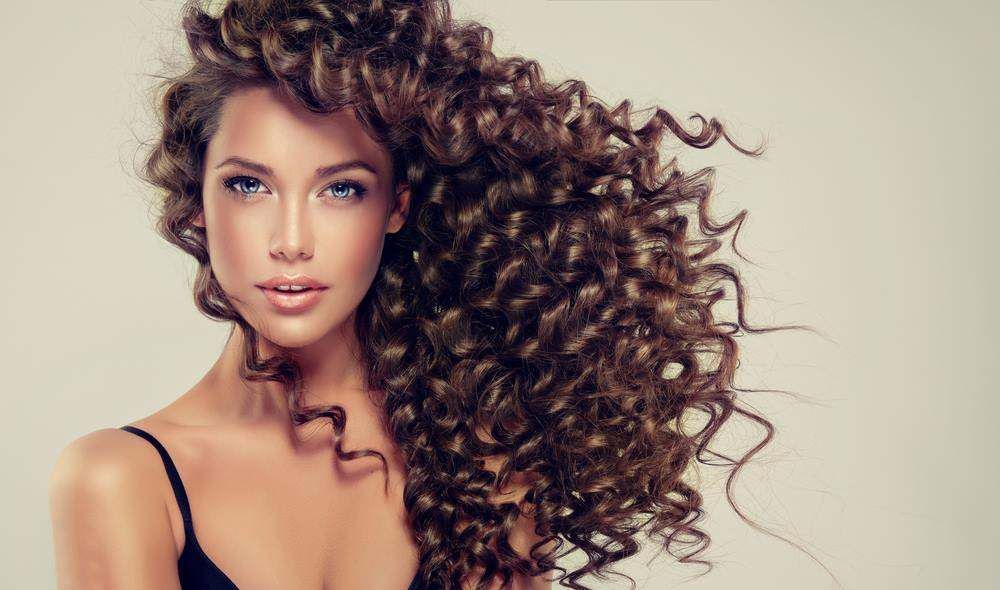 Woman with Voluminous Curly Brown Hair Against a Light Background — Fraser Shores Hair Design in Urraween, QLD