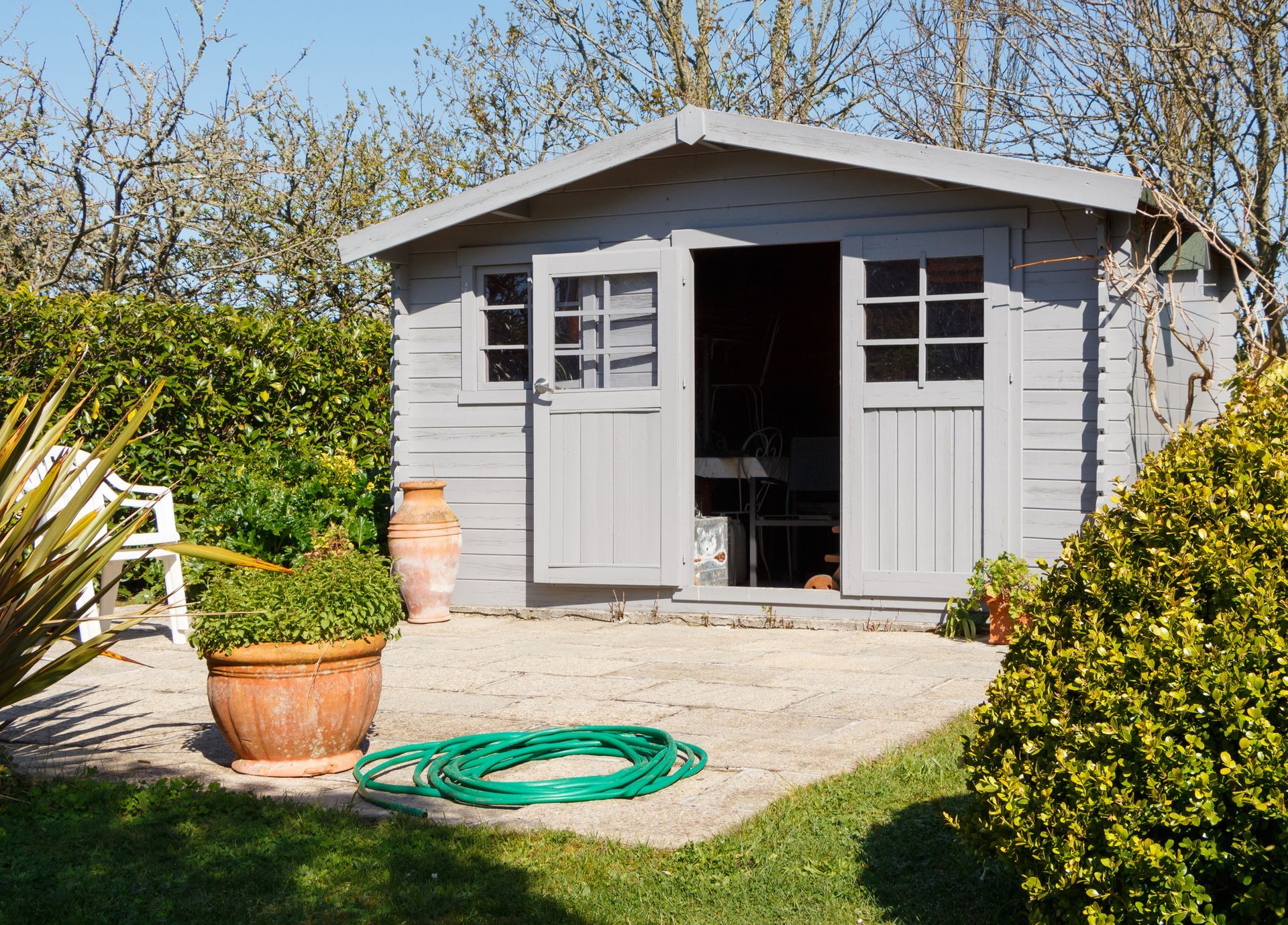 A garden shed with a green hose in front of it.