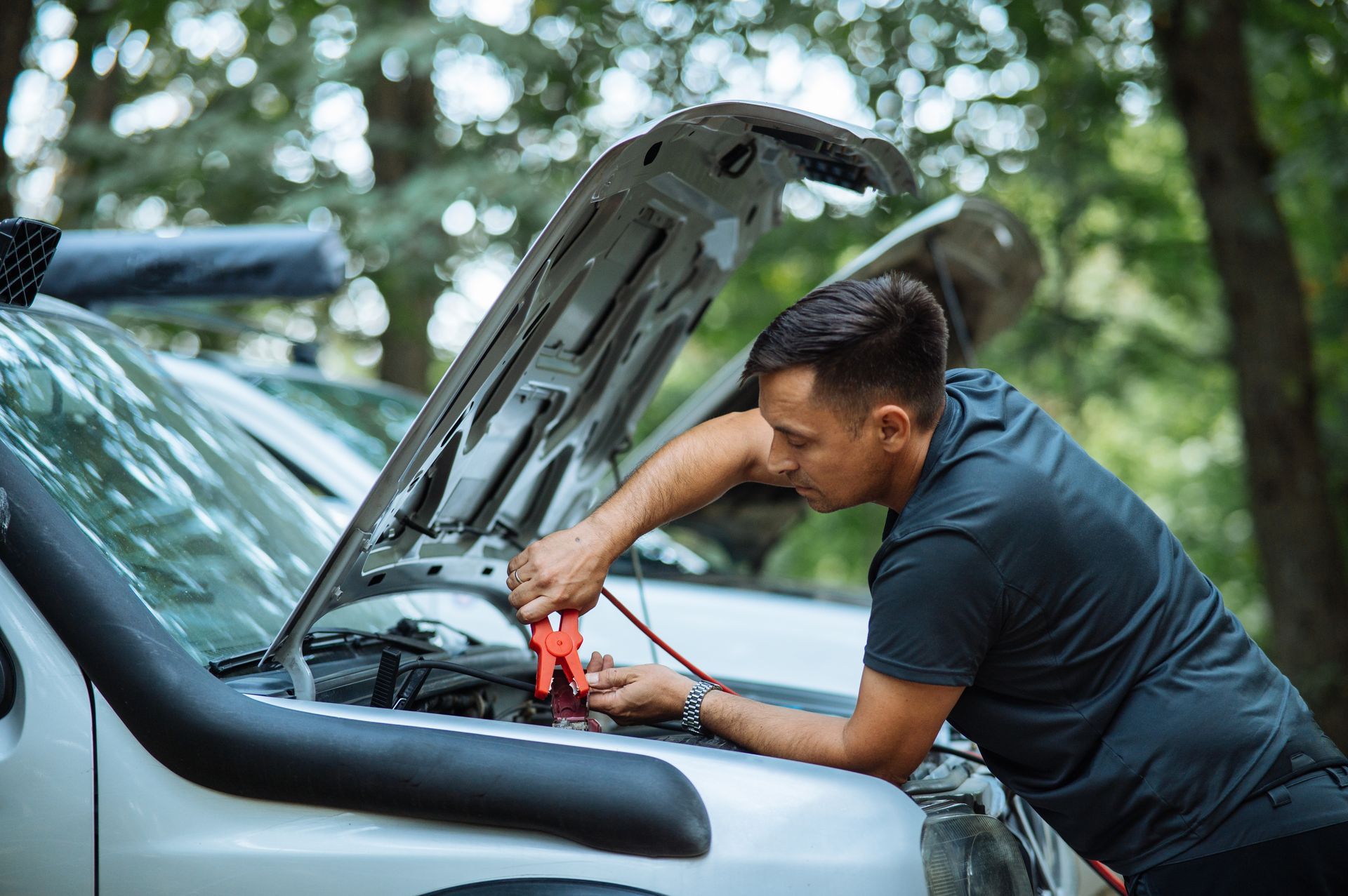 A man uses colored cables to jumpstart a car.