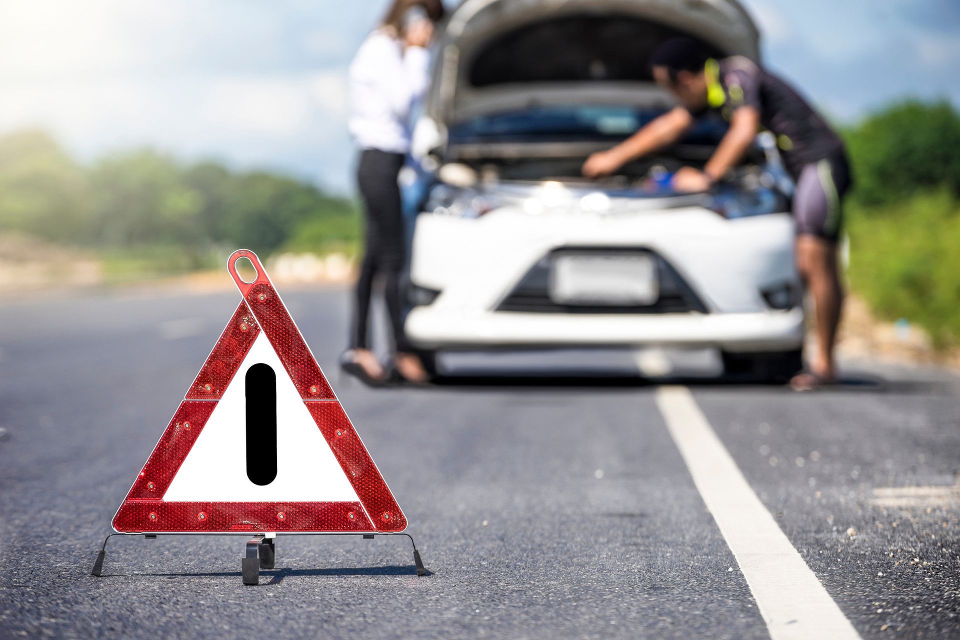 White car stopped with red emergency sign, showing need for roadside service.