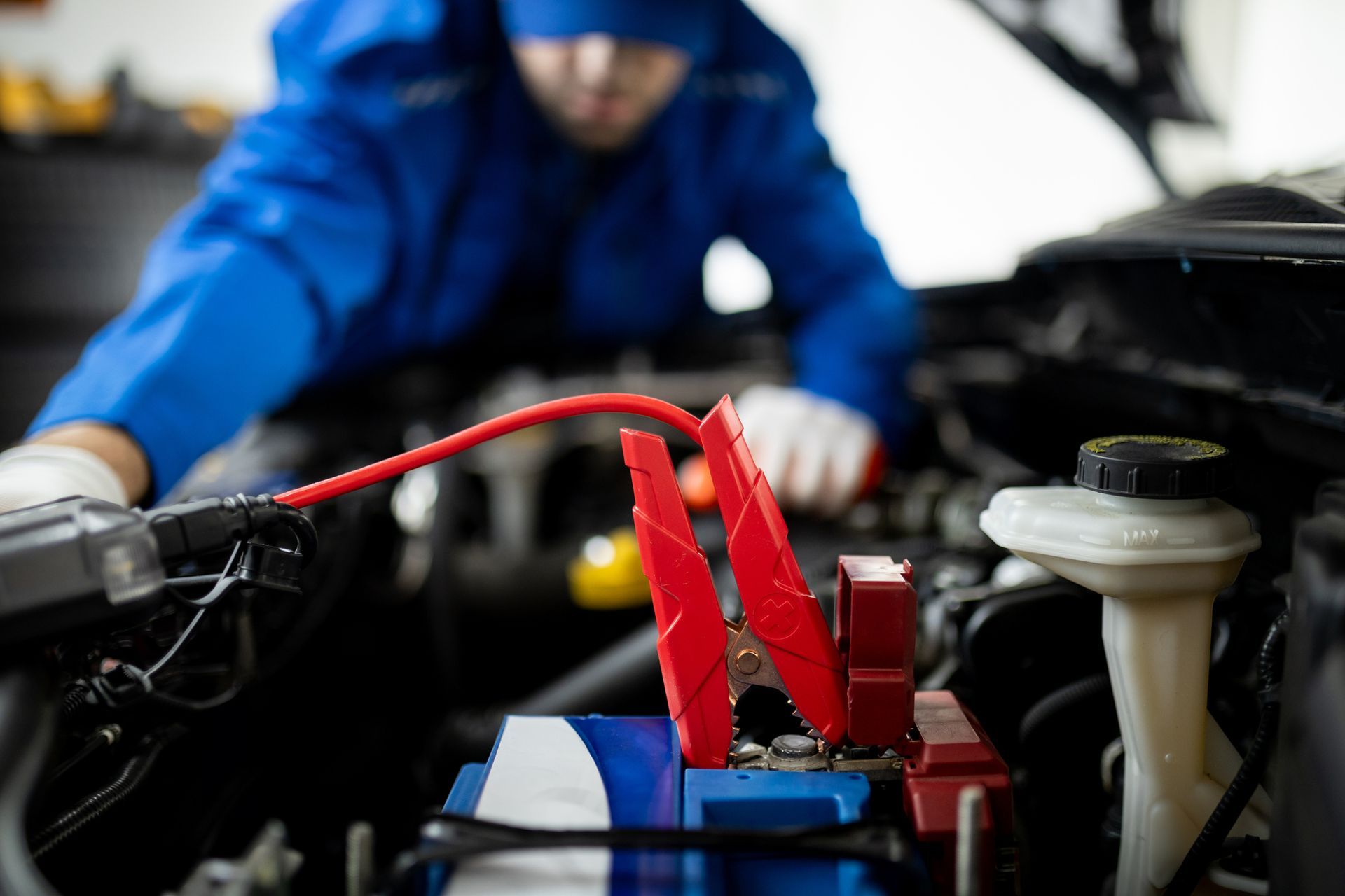 A mechanic performing an auto jumpstart with red jumper cables connected to the car battery.