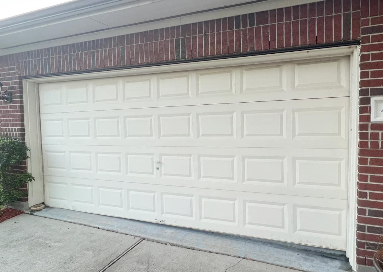 A white garage door is sitting in front of a brick house.