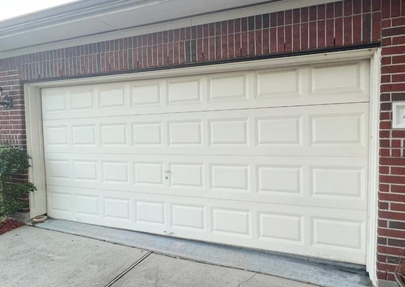 A white garage door is sitting in front of a brick building.