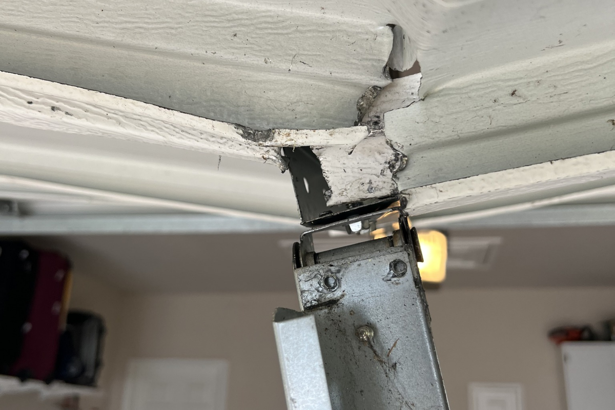 A close up of a garage door with a broken hinge.
