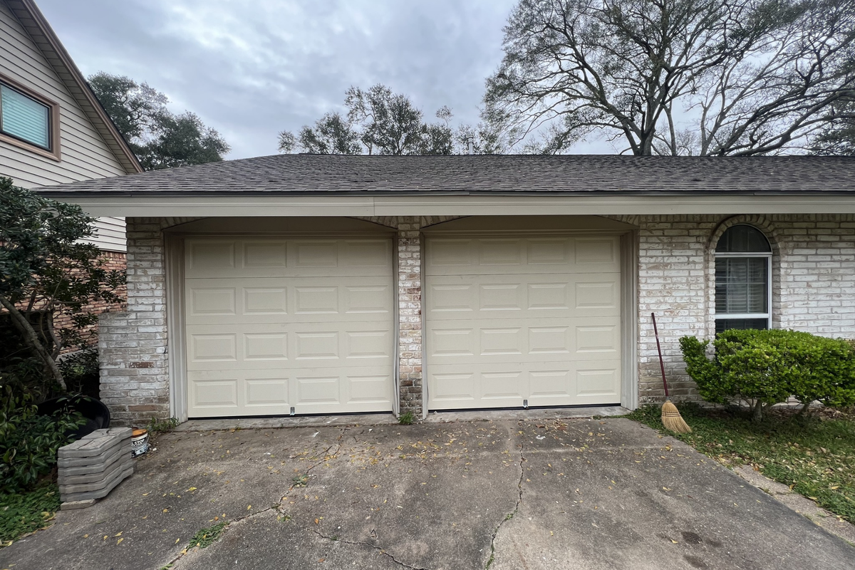 A white garage door is sitting in front of a brick house.
