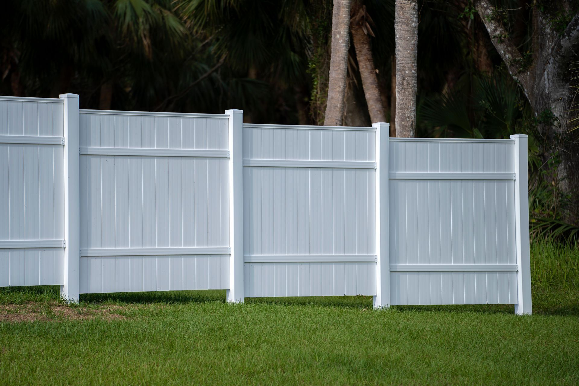 White vinyl picket fence on green lawn surrounding property grounds.