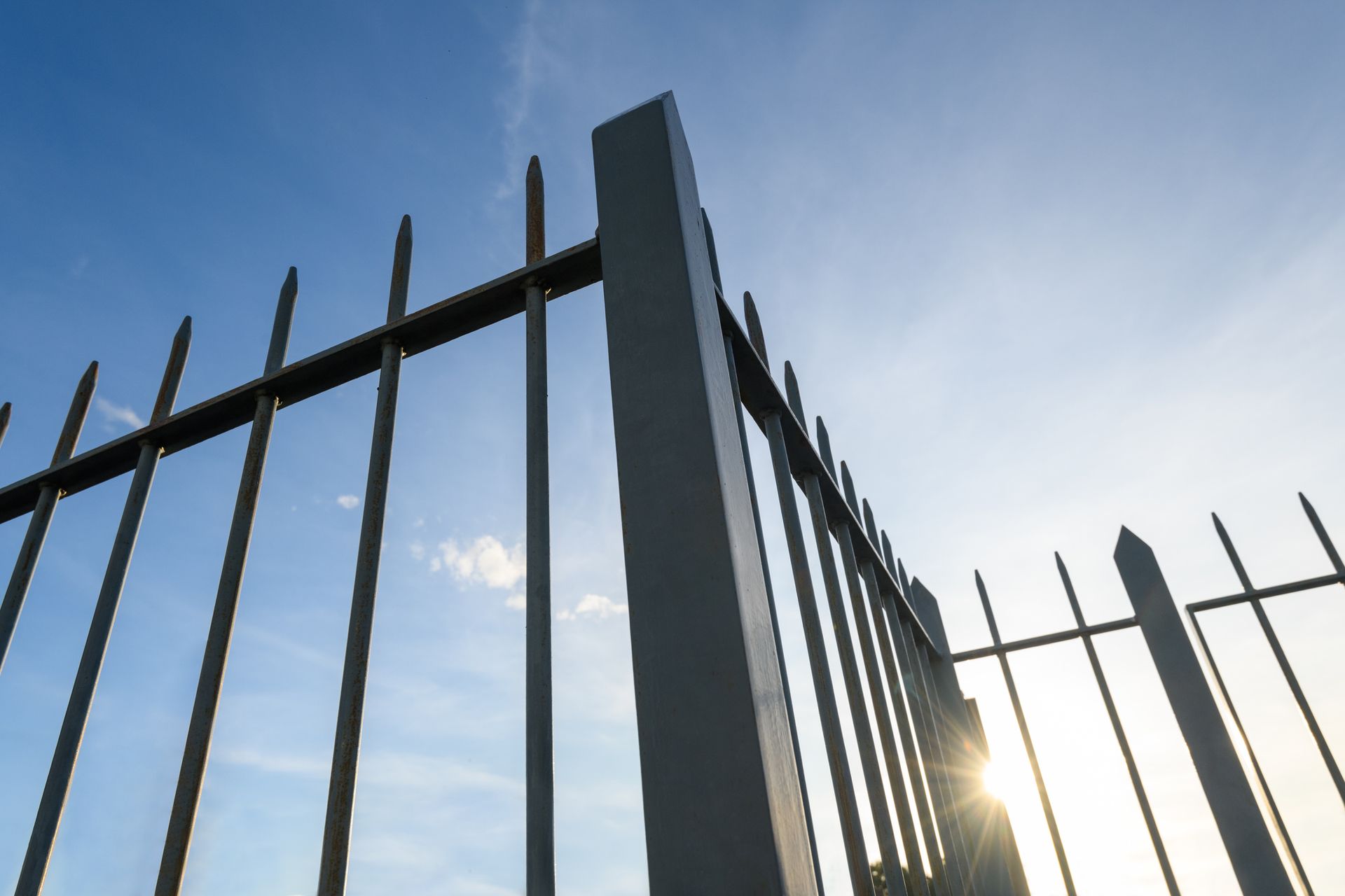 Close-up of metal fencing materials with pointed vertical bars against a blue sky.