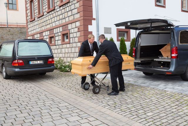 Tim Dölzer und ein Mitarbeiter bei Bestattungen Emmerling tragen einen Sarg zum Fahrzeug