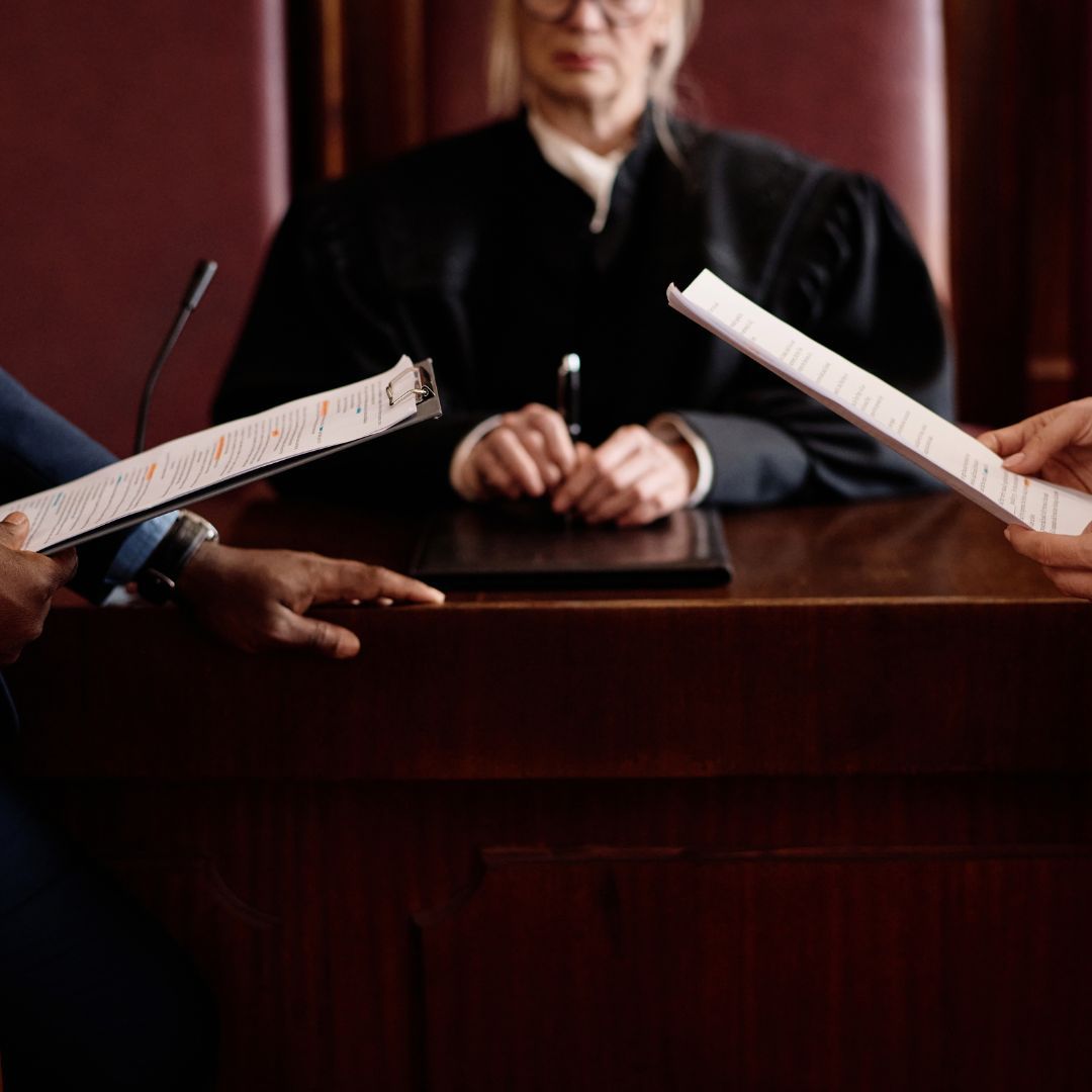 Lawyer at a courtroom bench as two hands hold legal documents in the foreground
