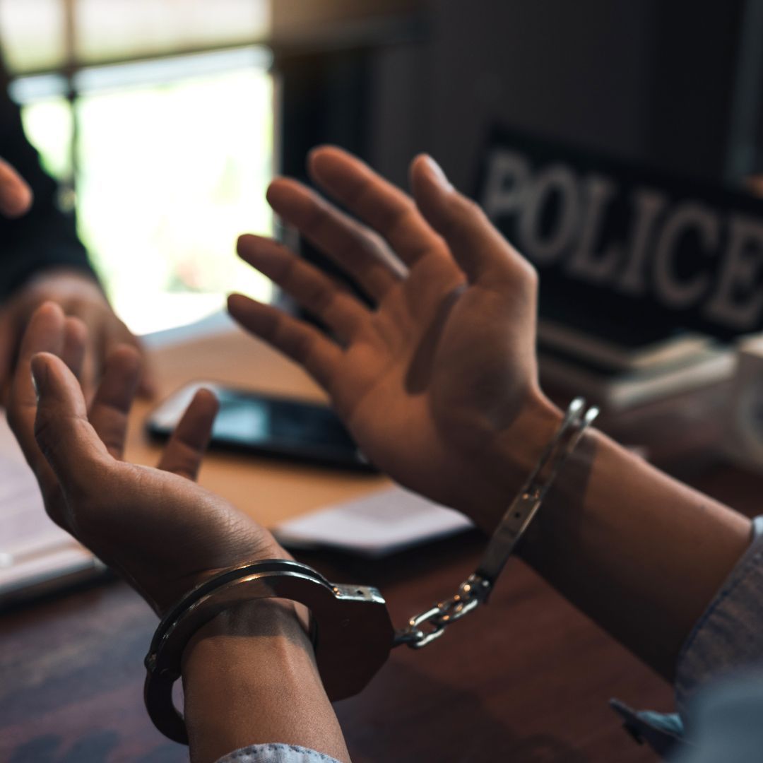 Handcuffed hands raised in a police interrogation room with a POLICE sign in the background