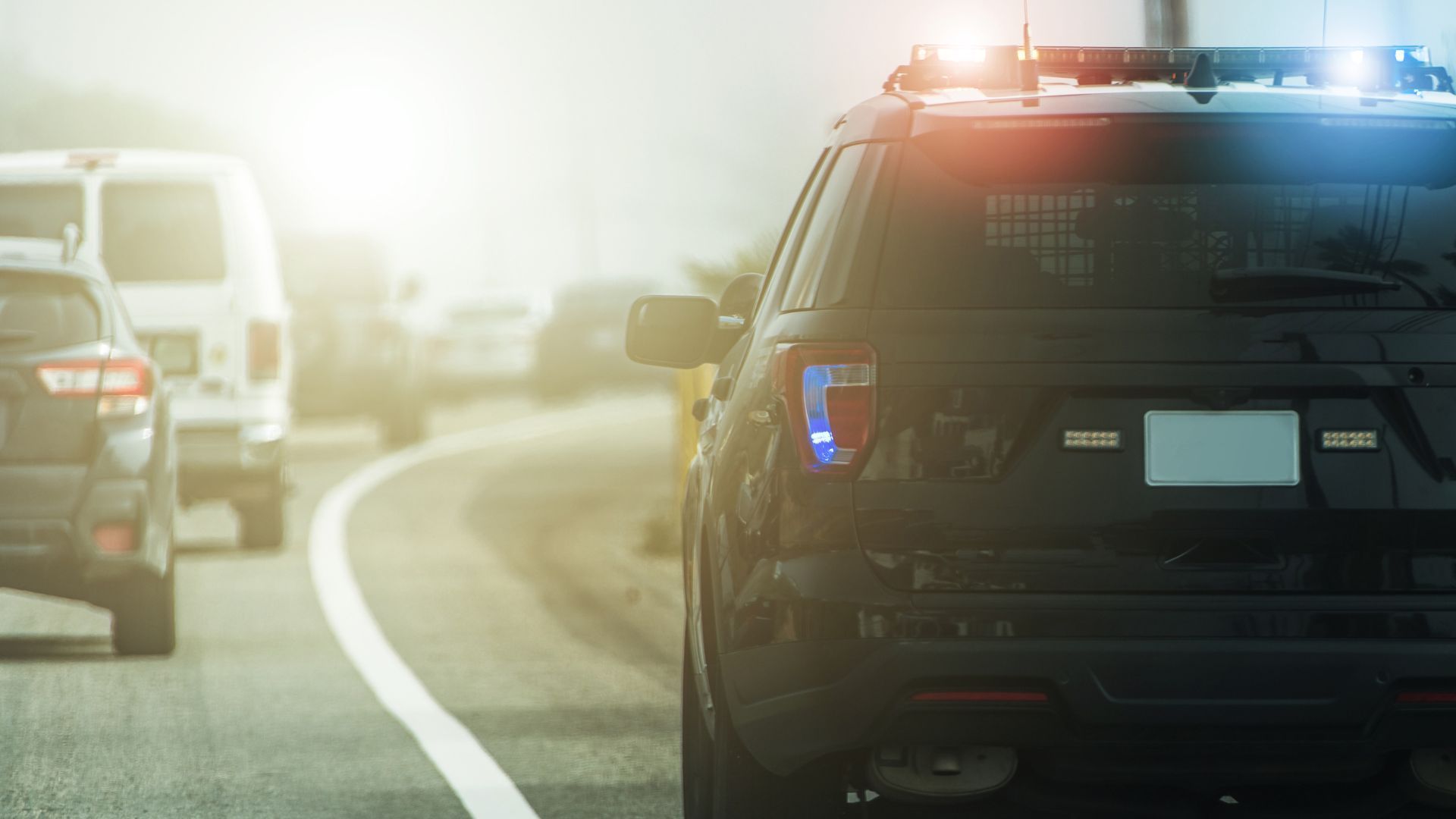 Police SUV with flashing lights on a foggy highway, other vehicles ahead in the distance