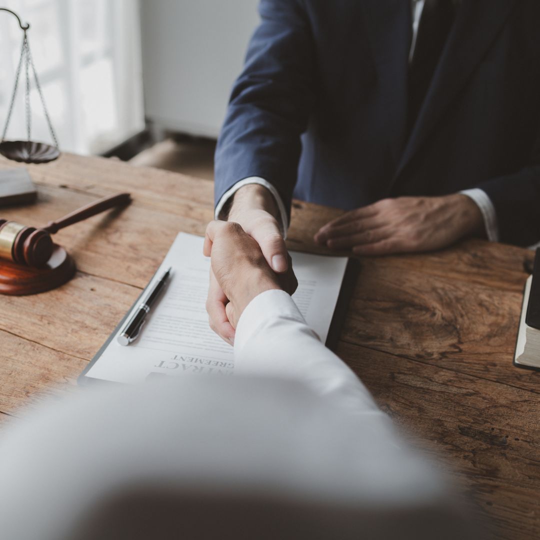 Handshake over a desk with a clipboard and pen, suggesting a business agreement.
