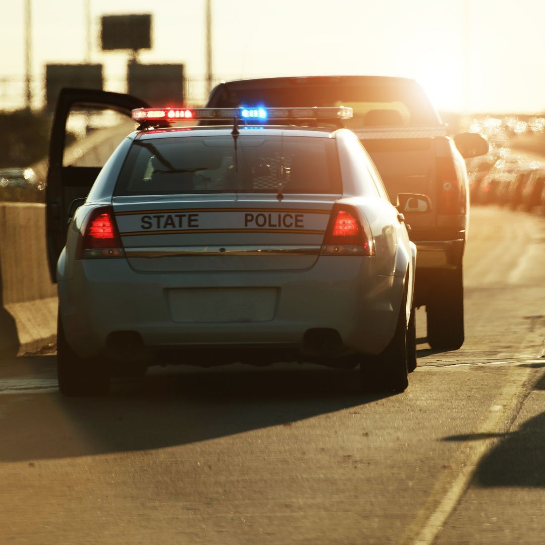 State police car with flashing lights pulling over a vehicle on a sunlit road