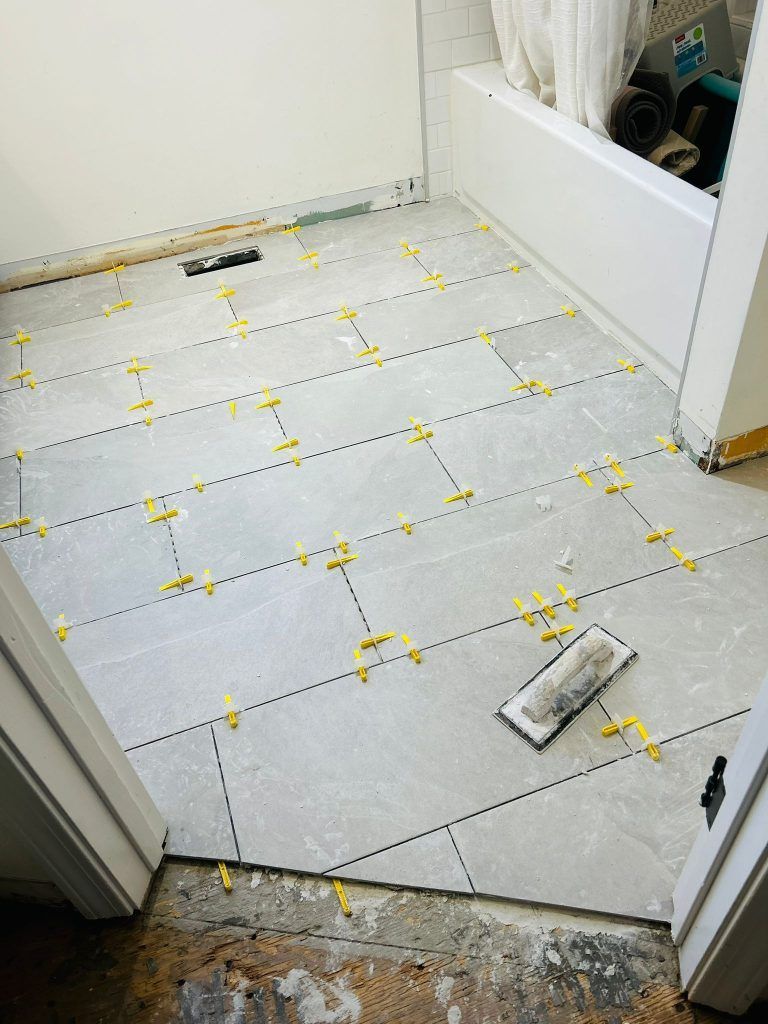 A bathroom floor with tiles being installed and a trowel on it.