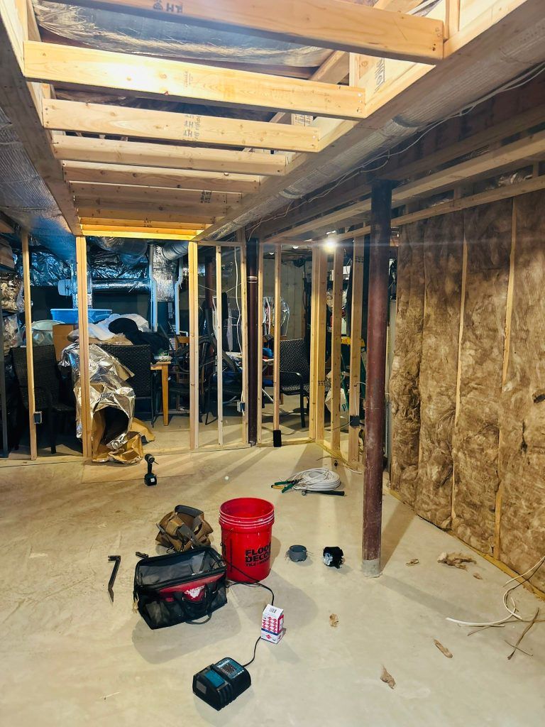 Basement under construction, framing and insulation visible. Tools and materials on the concrete floor.