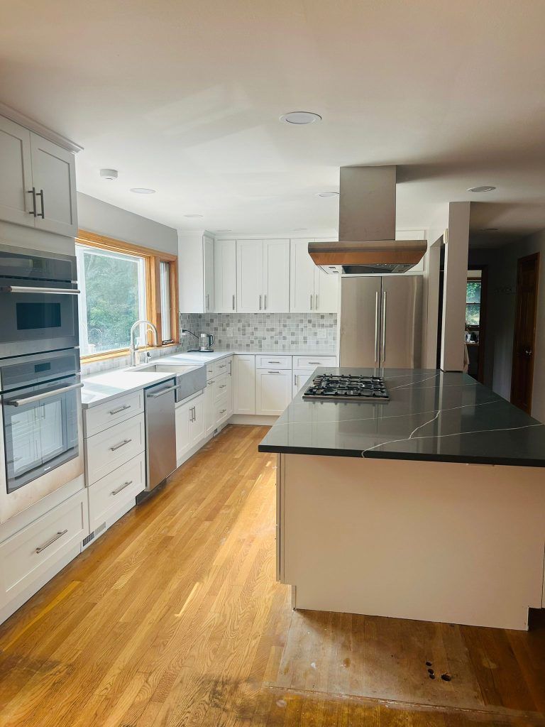 A kitchen with white cabinets , stainless steel appliances , and a large island.