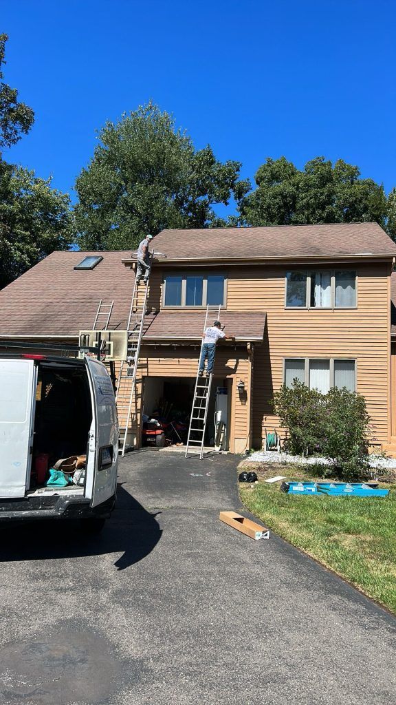 A man on a ladder is painting the roof of a house.