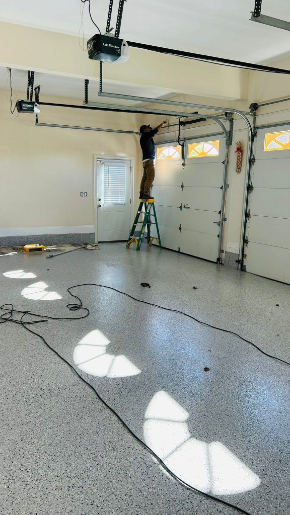 Man on ladder working on garage door opener in a freshly painted garage.