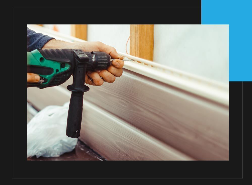 A man is using a drill to install siding on a wall.