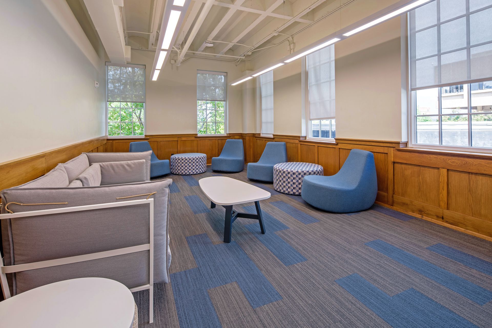 Lounge area with blue and gray furniture, carpet, and windows with light streaming in.
