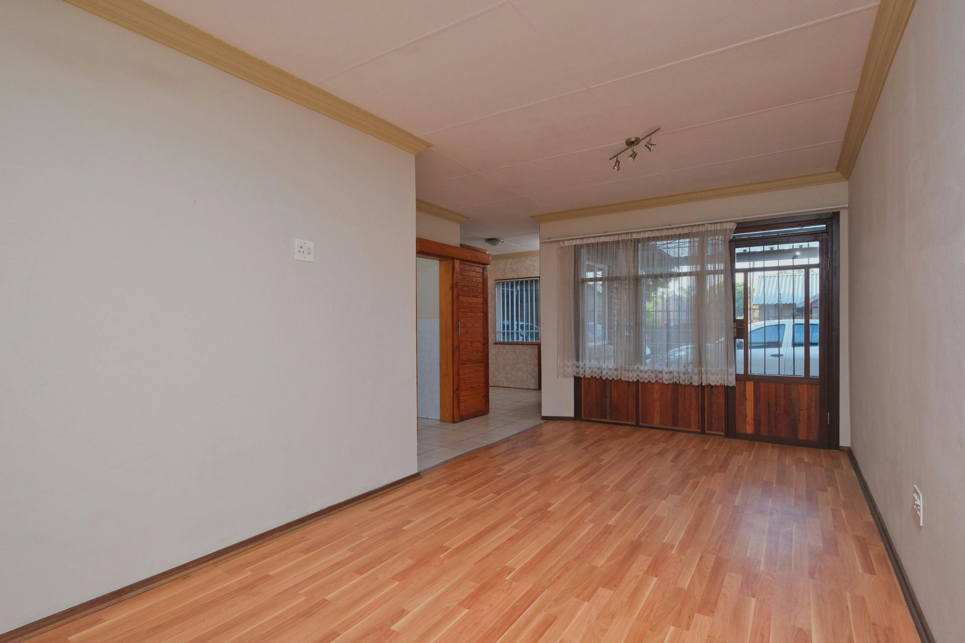 Bright, modern kitchen with white cabinets, wooden countertop, and gray tiled floor. Dining table and open doorway to living room.
