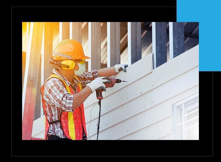 A construction worker is using a drill to install siding on a building.