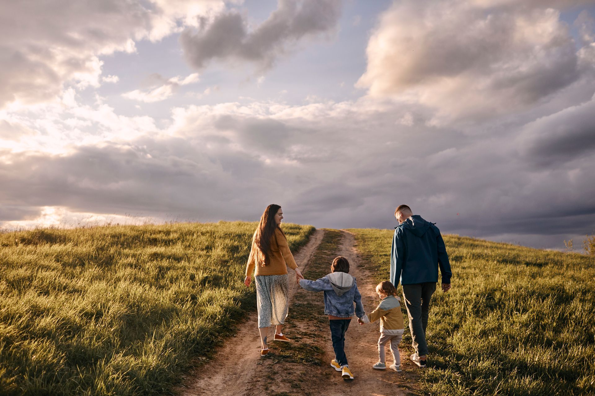 A family is walking down a dirt road holding hands.