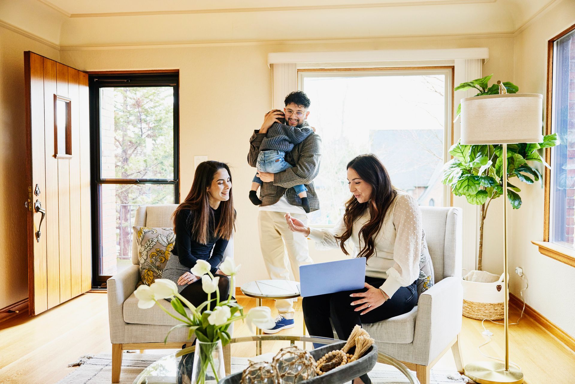 A group of people are sitting in a living room looking at a laptop.