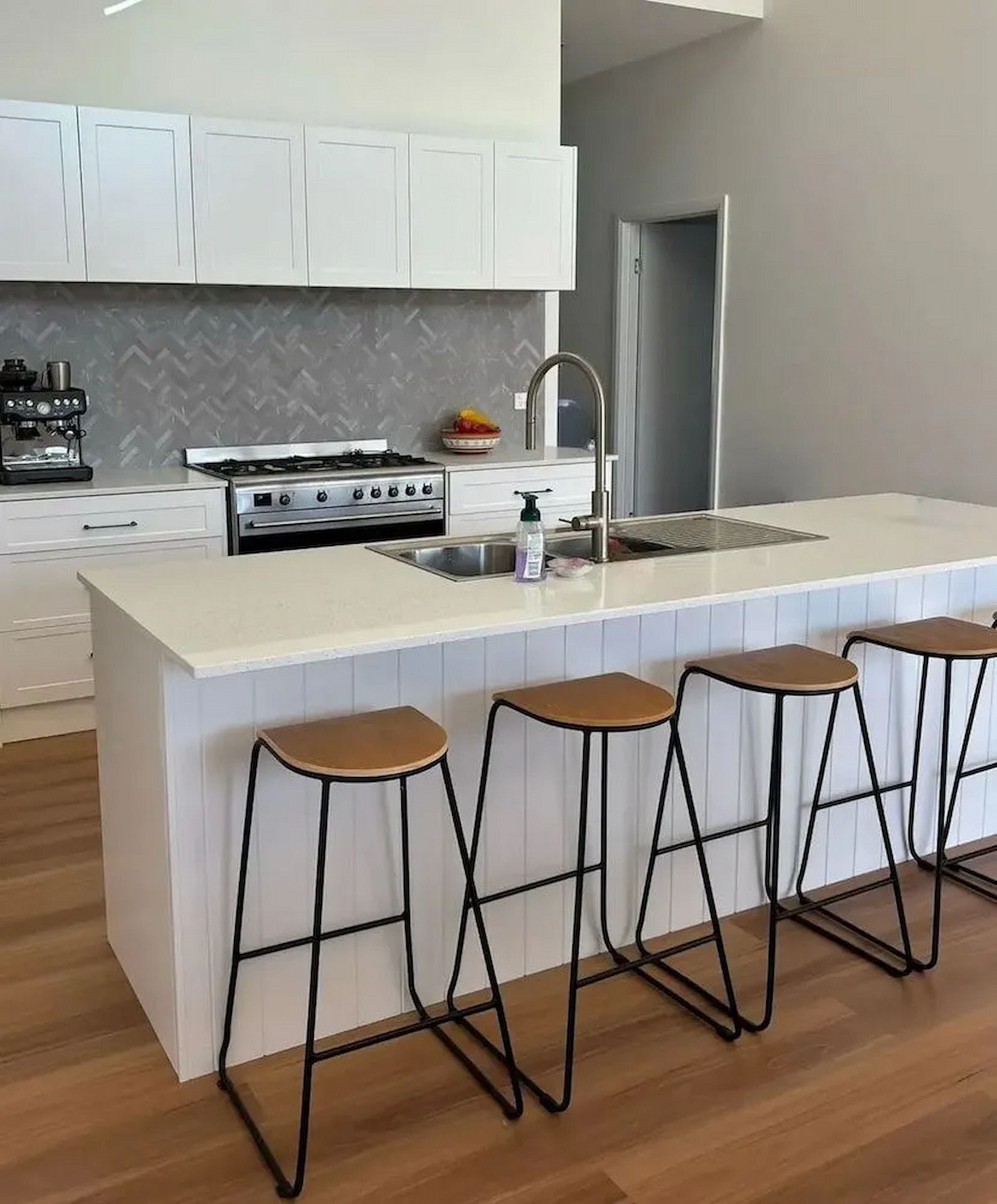 Modern kitchen with white cabinets, island with stools, stainless steel appliances, and wooden floor — Nielsen Construction in Wagga Wagga, NSW