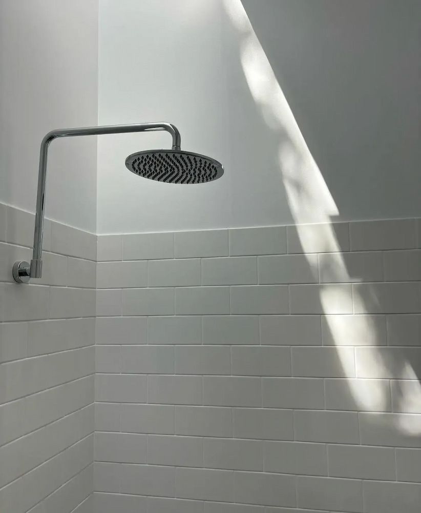 Shower Head With Sunlight Across White Tiled Wall — Nielsen Construction in Wagga Wagga, NSW