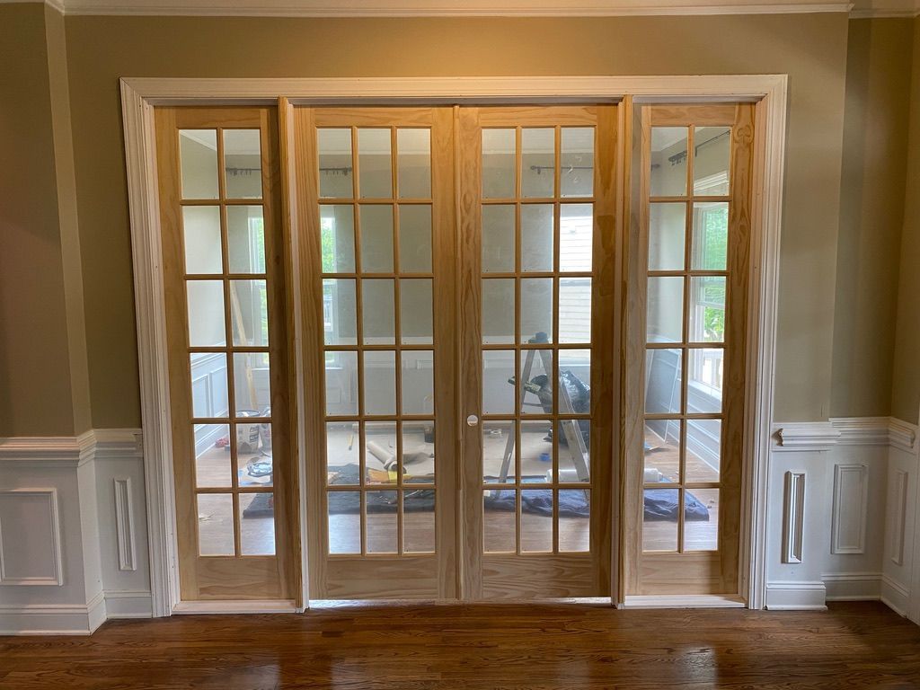 Four wooden French doors with glass panes, set in a room with light-colored walls, white trim, and a dark hardwood floor.