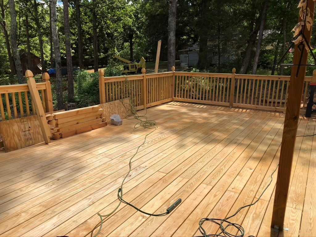 Wooden deck with a railing, in a wooded setting. A tangled electrical cord is across the deck.