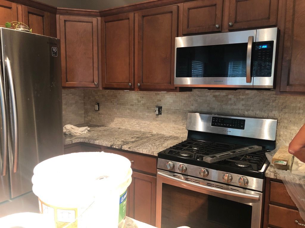 A kitchen with brown cabinets, stainless steel appliances, and granite countertops. A bucket sits in the foreground.