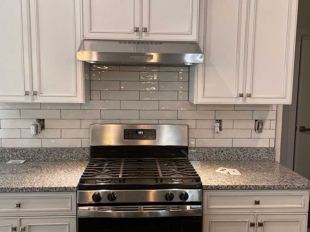 Kitchen with white cabinets, stainless steel appliances, and gray countertops. White subway tile backsplash and range hood above the stove.