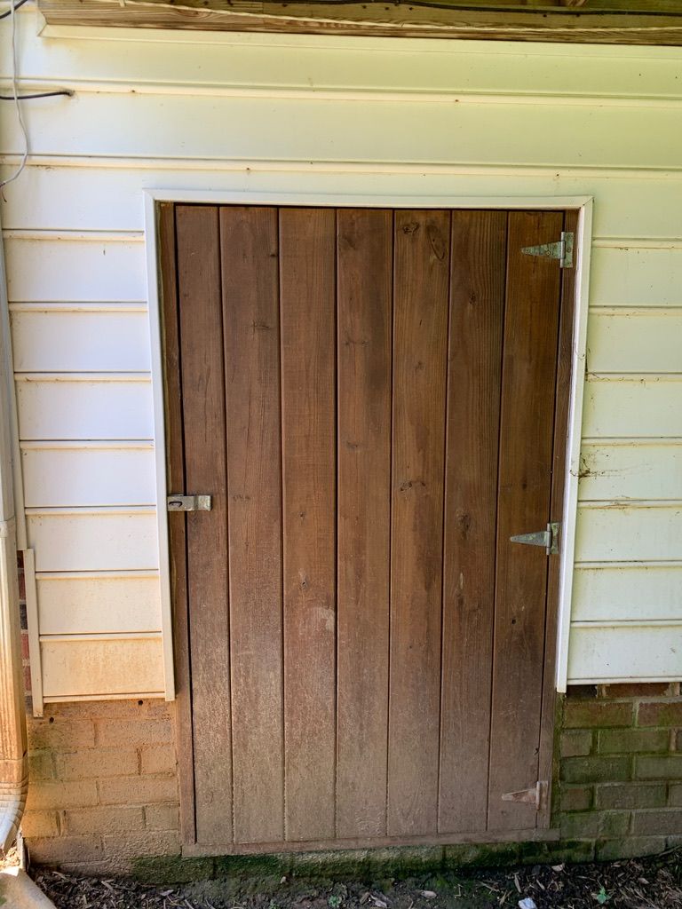 Wooden door in a white-framed opening on a building with white siding and a brick base.